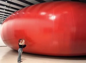 Giant Red Balloon with a Woman Taking Photos Next to it - Anish Kapoor Exhibition at Hayward Gallery London